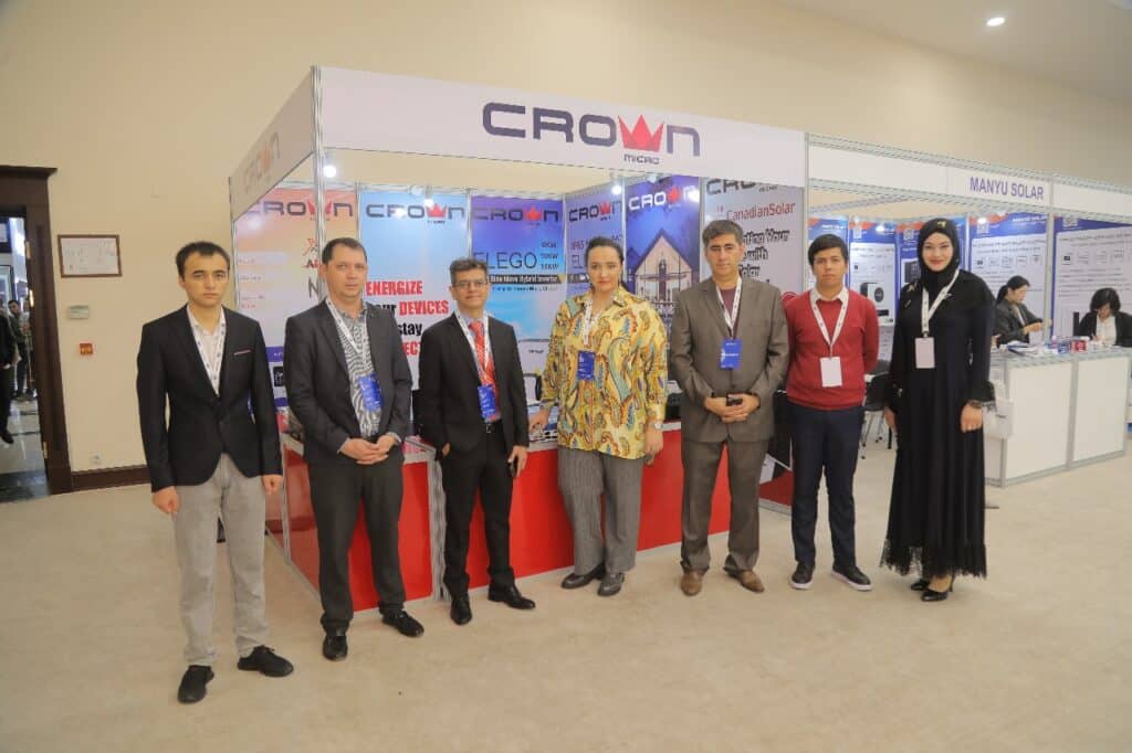 Seven professional team members posing in front of a Crown Micro solar energy trade show booth display.