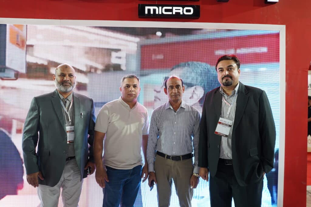 Four professional men standing side by side in front of a Crown Micro digital banner at a trade show event.