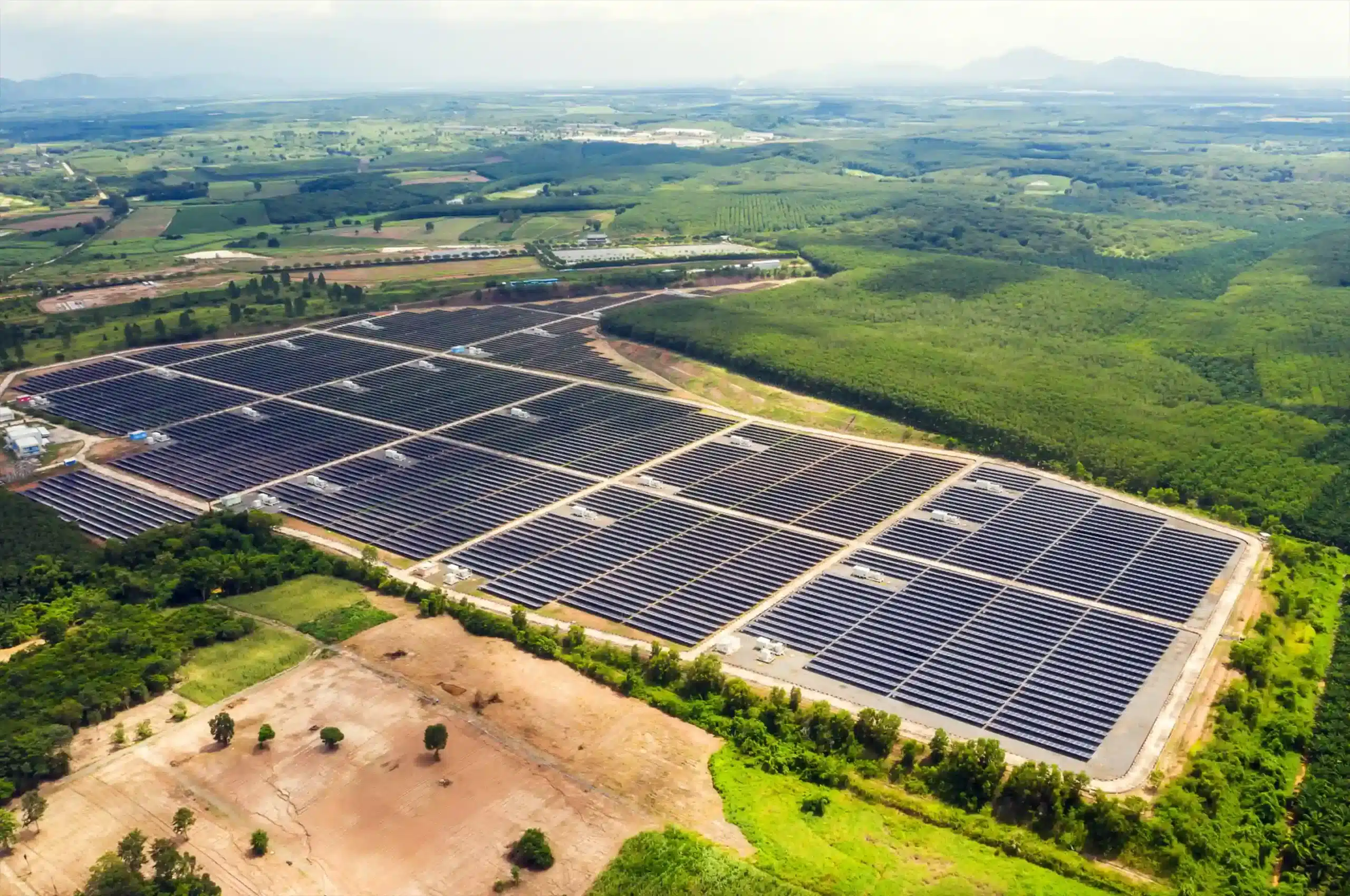 Aerial view of a massive industrial solar farm with thousands of panels organized in grid blocks across a rural landscape.