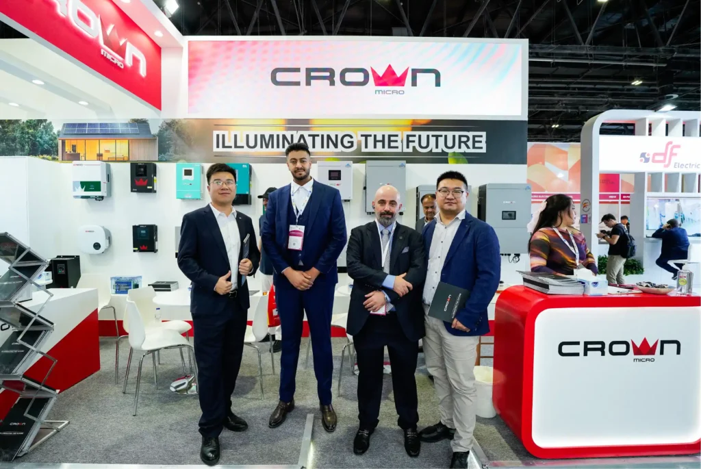 Four professional men standing together in front of a Crown Micro solar exhibition booth displaying smart inverters.
