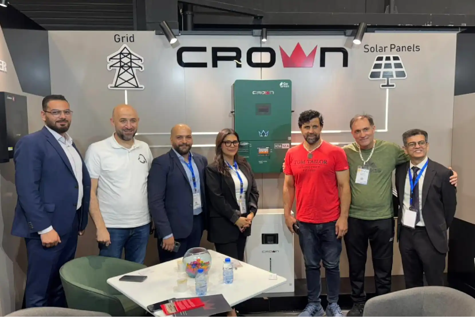 Seven professional attendees smiling at a clean energy trade exhibition booth featuring a large Crown logo banner.