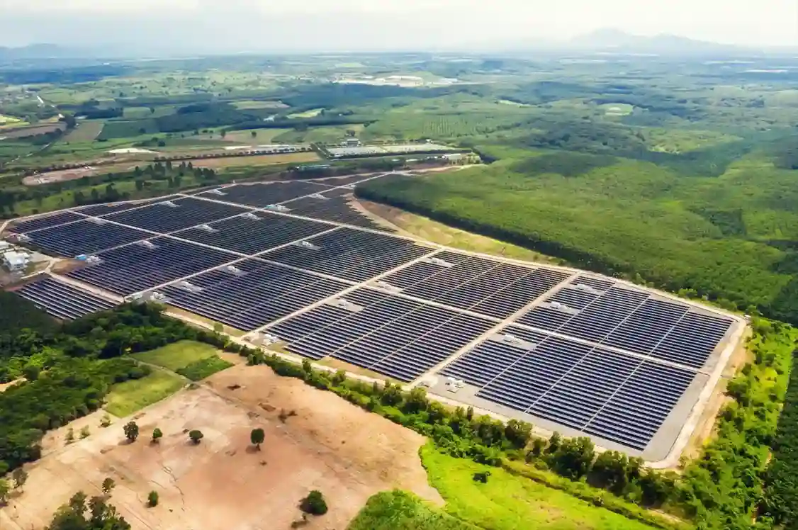 Aerial view of a massive industrial solar farm with thousands of panels organized in grid blocks across a rural landscape.